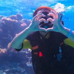 A girl in scuba diving near a sea reef, shows a heart with her hands